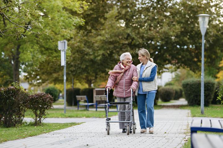 Una mujer mayor y su cuidadora paseando por el parque