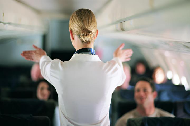 Vista trasera de una azafata explicando la seguridad del avión a los pasajeros