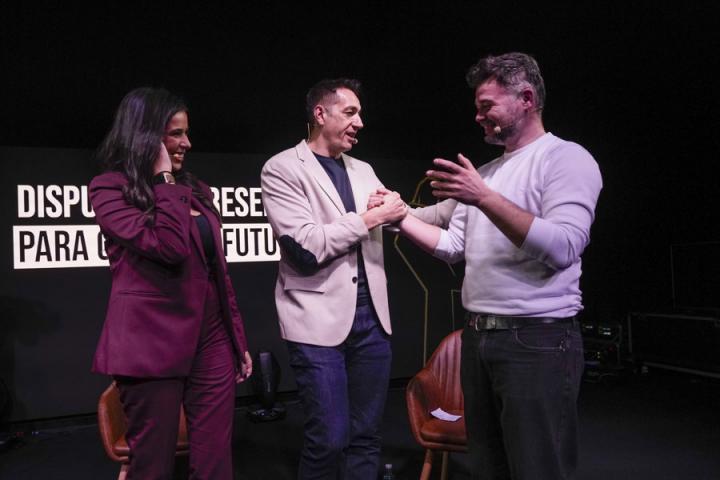 Gabriel Rufián y Emilio Delgado se saludan durante su acto por la unidad de la izquierda en presencia de la moderadora, Sarah Santaolalla