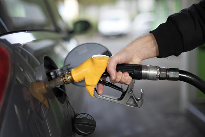 La mano de un hombre echando combustible en su vehículo con una bomba de gasolina amarilla.