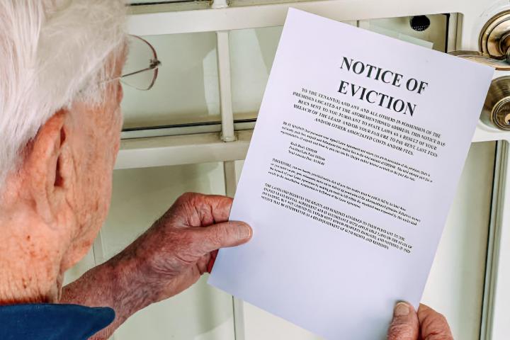 Un hombre mayor sosteniendo un aviso de desalojo en la puerta principal de una casa
