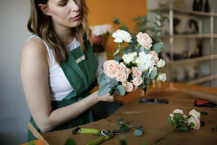 Una mujer haciendo un ramo de flores y papel artesanal en una floristería