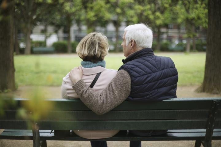 Una pareja de ancianos sentada en un banco público en un jardín público.