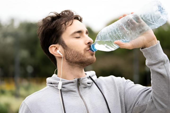 Primer plano de un joven con los ojos cerrados bebiendo agua y escuchando música en el parque
