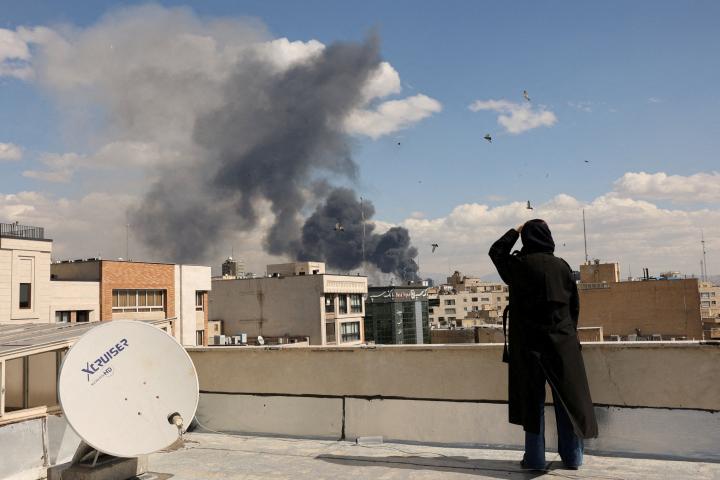 Una mujer, desde una terraza, ve el humo de los bombardeos en Teheran