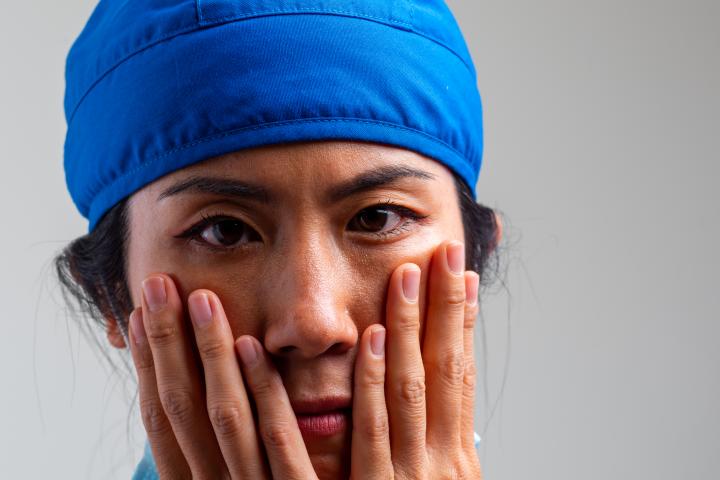 Trabajadora de la salud, adulto de mediana edad, seria, con exceso de trabajo y estresada, mirando a la cámara sobre un fondo gris