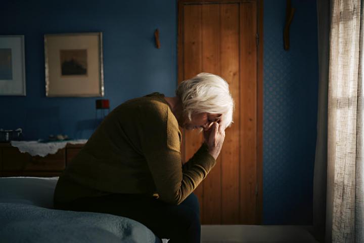 Una mujer mayor preocupada sentada en la cama con la cabeza agachada