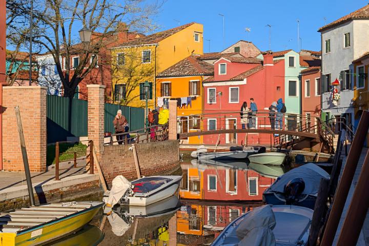 La gente caminando por una pasarela sobre el canal con barcos amarrados en Burano