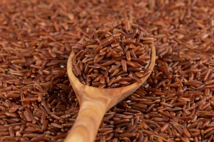 Red rice in a wooden spoon on red rice background