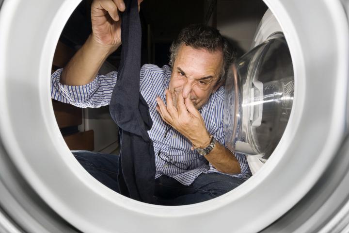 Un hombre cogiendo un calcetín que huele mal en la lavadora