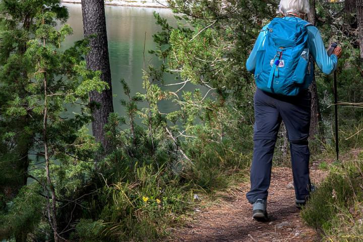 Una señora mayor con una mochila caminando con bastones de trekking por un sendero en el bosque