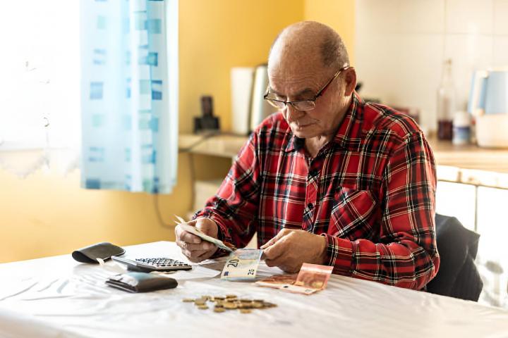 Un hombre mayor contando dinero en moneda de la Unión Europea