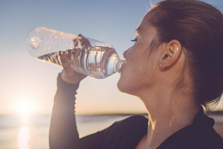 Una mujer bebiendo agua junto al mar