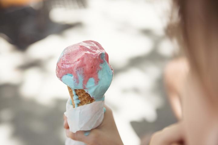 Helado rosado y azul derritiéndose en un cono y sostenido por un niño.