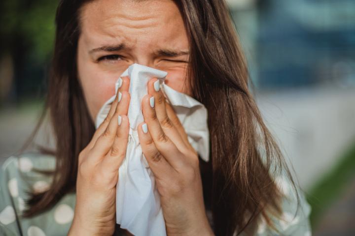 Primer plano de una joven que se suena la nariz con un pañuelo. Fondo borroso.