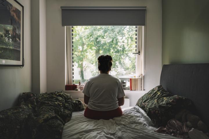 Mujer de espaldas en su habitación, viendo hacia la ventana.
