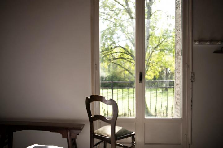 Una silla antigua de madera frente a una ventana con vistas al jardín.