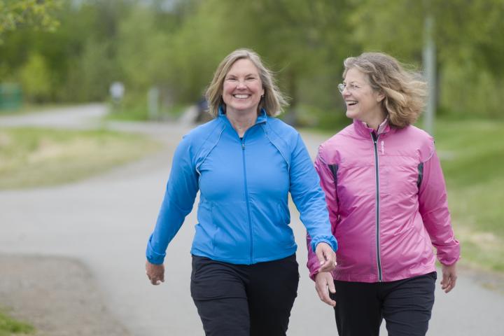 Dos mujeres mayores de sesenta y tantos años haciendo ejercicio caminando juntas por un sendero pavimentado.