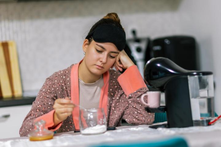 Una joven añade azúcar a su café en casa, preparando su bebida matutina con cuidado