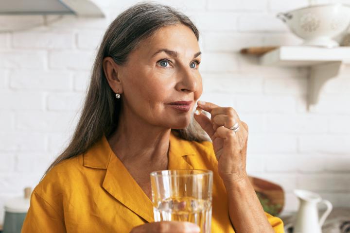 Mujer madura y atractiva sosteniendo medicamentos y un vaso de agua en las manos. Mujer mayor tomando medicamentos.