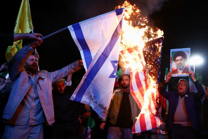 Un hombre sostiene una foto del líder supremo de Irán, Mojtaba Lamenei, mientras se queman banderas de EEUU e Israel, el 8 de abril de 2026 en Teherán, tras conocerse el alto el fuego en Irán.