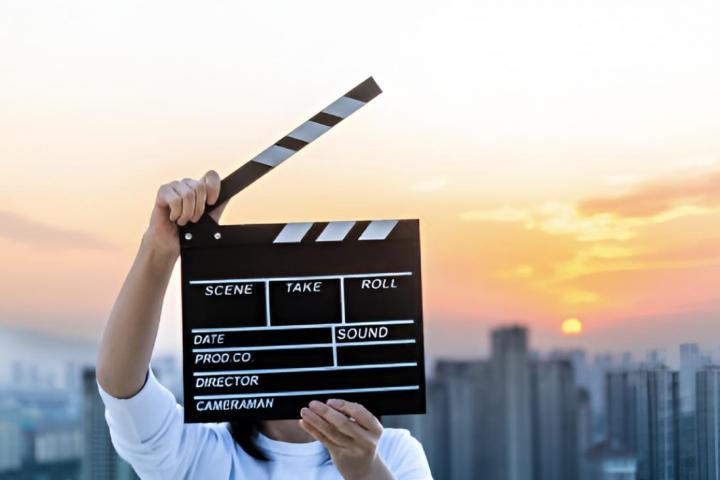 Una mujer sosteniendo una claqueta de una película con un atardecer de fondo.