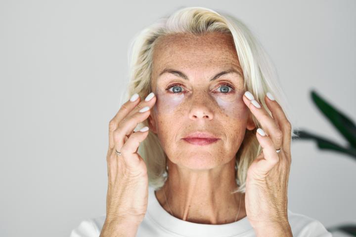 Mujer mayor con cabello plateado se aplica parches de hidrogel para el contorno de ojos,