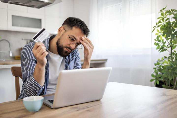 alt="alt="Un hombre con una tarjeta de crédito en la mano frente a un ordenador con cara de tensión""