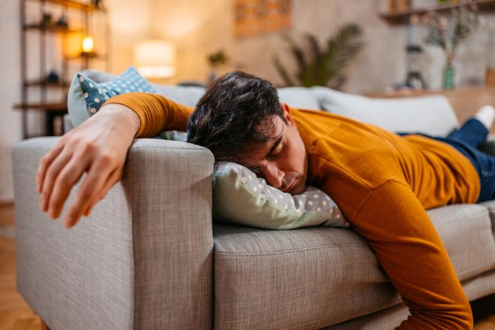 Un joven cansado se queda dormido en el sofá del salón.