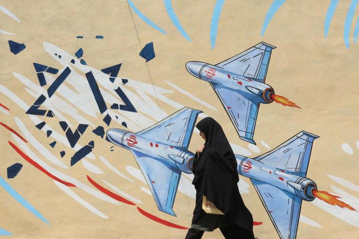 Una mujer iraní con velo pasa junto a un mural antiestadounidense y antiisraelí en una calle de Teherán, el 20 de abril de 2026.