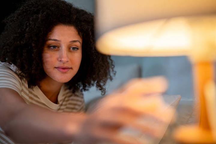 Attractive Latina woman turning off the light in bedroom at night before sleep. Young female feeling happy and relaxed, resting and enjoying a peaceful holiday weekend at home in a dark room.