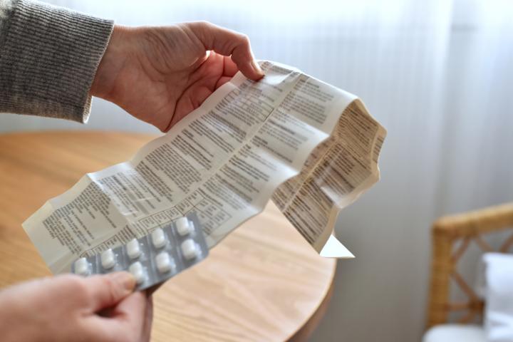 Manos sosteniendo un blíster con pastillas y un folleto informativo para el paciente.