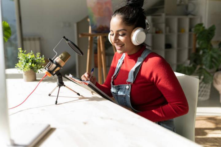 alt="alt="Attractive smiling woman in red sweater sits at home recording a podcast""