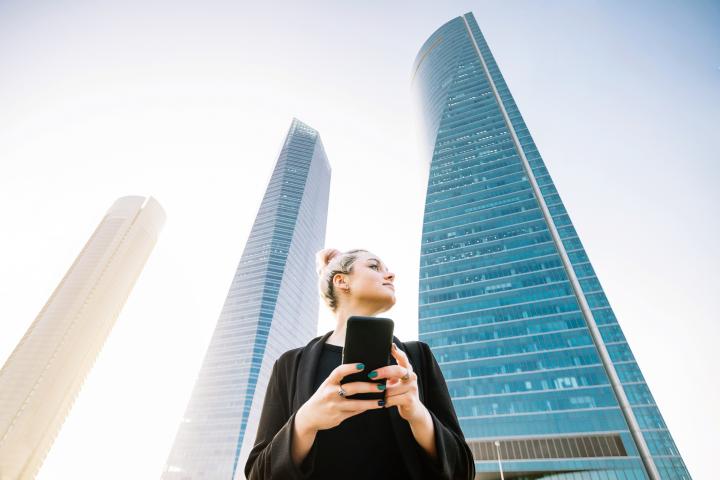 Horizontal mid waist view of blonde young woman typing on phone in financial city in Madrid. People and business lifestyles