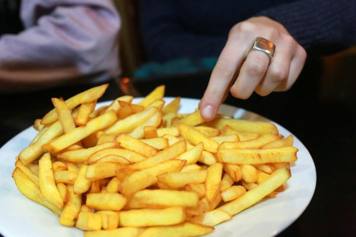 Manos de una persona comiendo de un plato de patatas fritas en un bistró parisino.