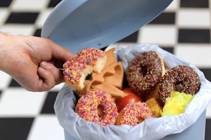 Una persona tirando donuts y otros alimentos ultraprocesados a la basura.