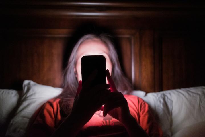 Mujer viendo el móvil acostada en la cama.