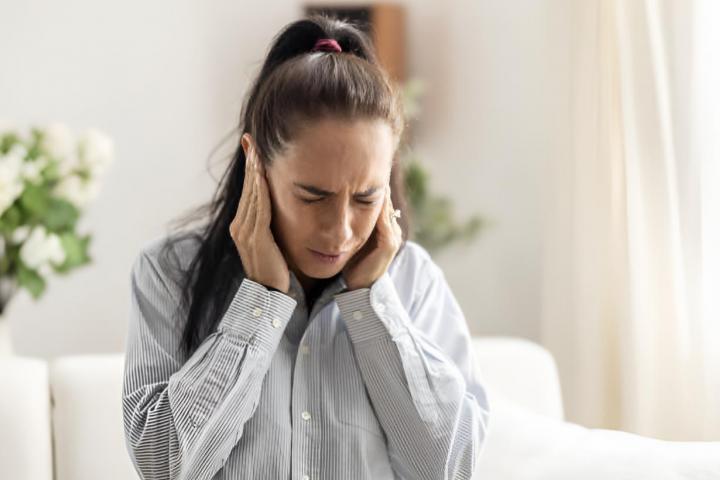 Una mujer tapándose los oídos con mueca de dolor
