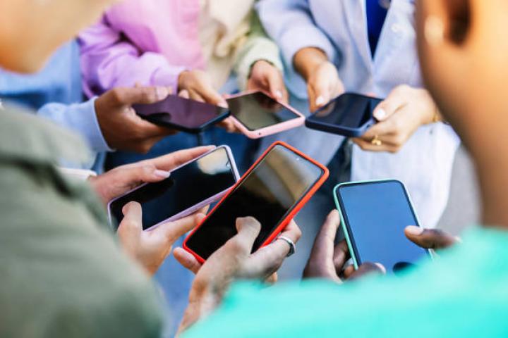 alt="alt="Young group of people standing in circle using mobile phones outside. Unrecognizable teen friends watching social media content on smartphone app. Technology lifestyle concept.""