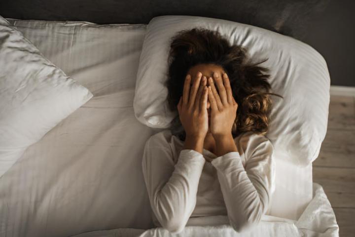 Chica triste y sola en su habitación con las manos en la cara y con insomnio y problemas psicológicos.