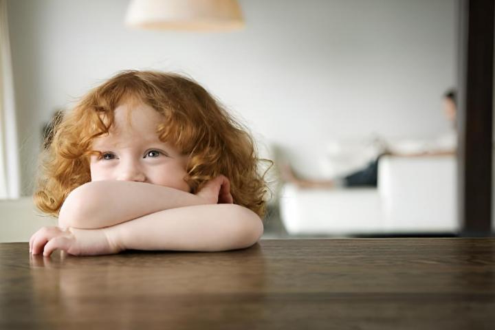 Una niña pequeña pelirroja apoya los brazos sobre una mesa de café.