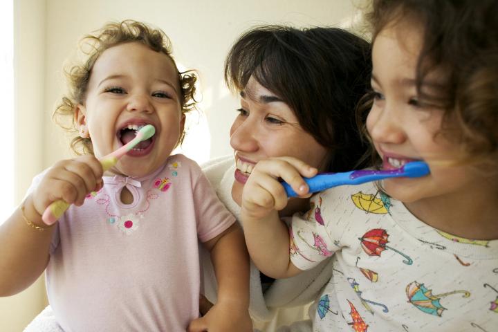 Madre ayudando a sus hijas a cepillarse los dientes