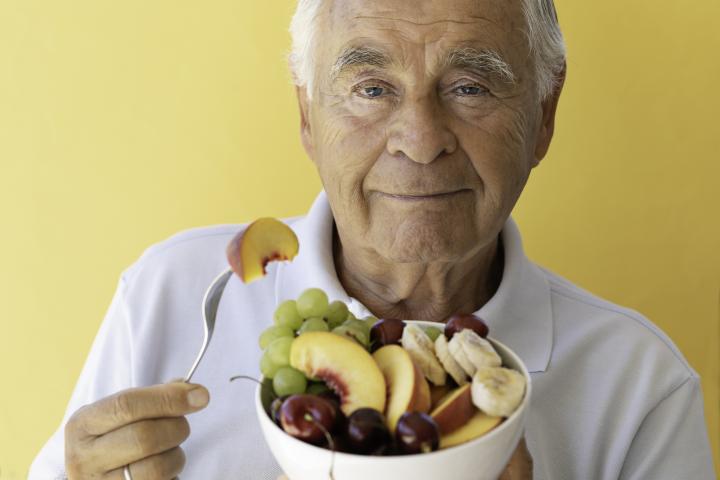 Vista frontal de un hombre mayor comiendo ensalada de frutas. Fondo de color naranja. Concepto de alimentación saludable.
