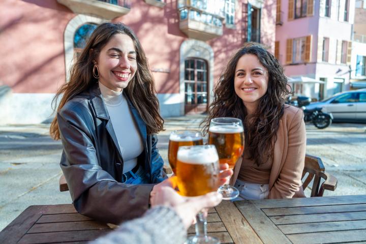 Grupo de mujeres disfrutando de bebidas y brindando con cerveza en la soleada terraza de un bar