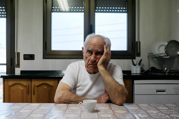 Un hombre mayor aburrido sentado en una silla de su cocina.