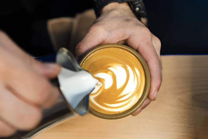 Barista elabora hábilmente el arte del café con leche vertiendo leche cremosa en una taza de café recién hecho, creando diseños y patrones intrincados.