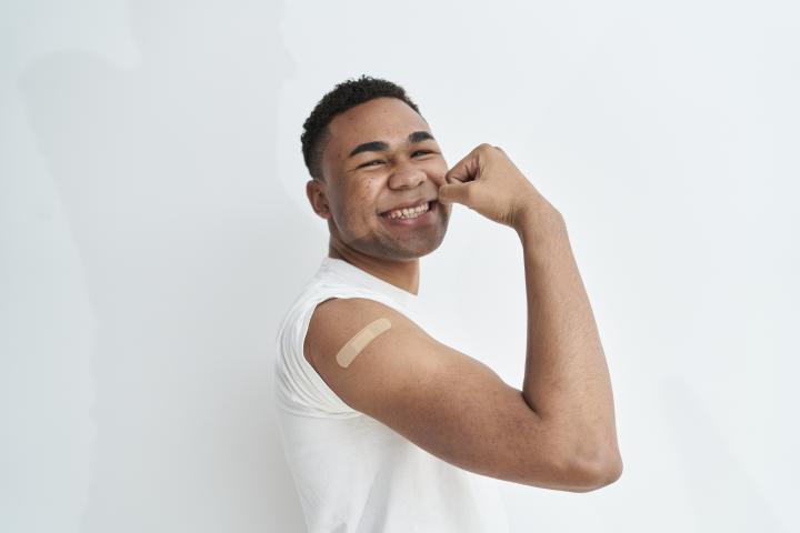 Short haired man wearing a white shirt smiling and flexing his arm, with a white background. Wellness concept