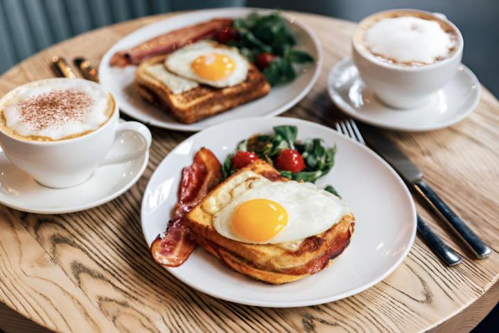 Un desayuno de dos cafés y dos tostadas con huevo y bacon