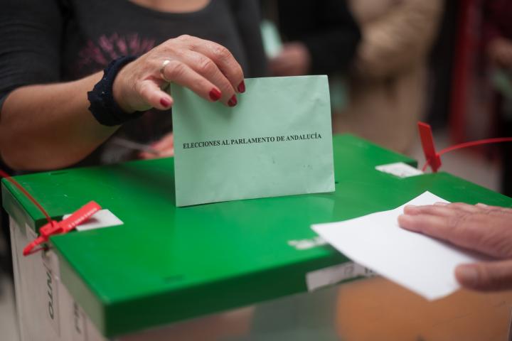 Urna de las elecciones al Parlamento de Andalucía con una mano votando.