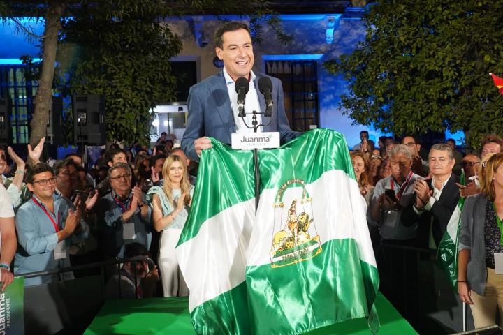 Subido en un escenario, rodeado de simpatizantes del PP, Juanma Moreno Bonilla sostiene una bandera de Andalucía